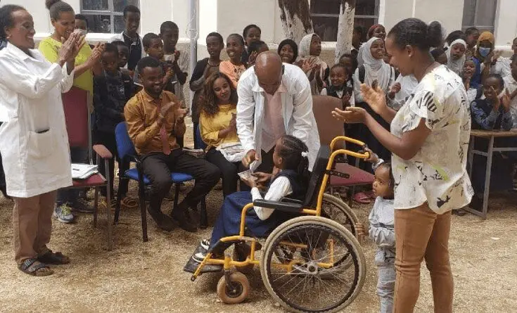 A group of people standing around a child in a wheel chair.